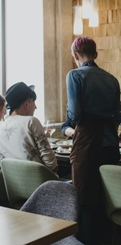 На фото изображено кафе, где официант принимает заказ у клиента