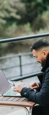 Фото мужчина общается через ноутбук сидящий на улице напротив реки