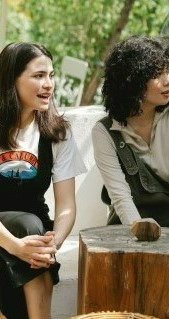 На фото две девушки сидящие в уличном кафе и обсуждая интересные ситуации