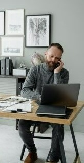 На картинке мужчина работает на ноутбуке у себя дома