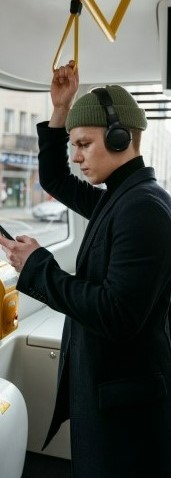 На картинке парень в троллейбусе изучает английский язык через телефон и наушники