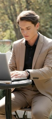 Фото, где молодой человек сидит в уличном кафе и учит через ноутбук английский язык