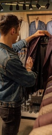 Фото на котором парень рассматривает пиджак в магазине
